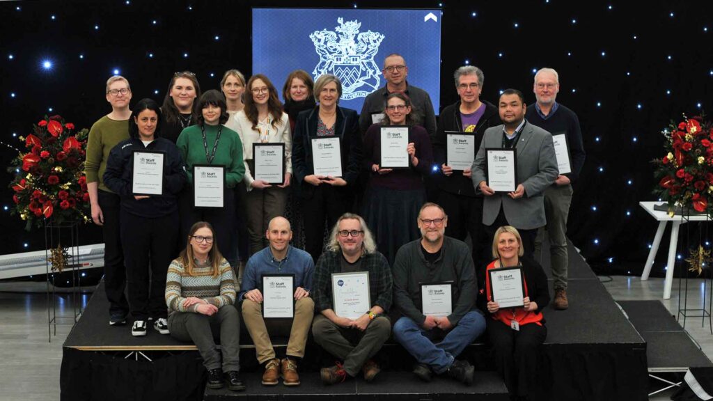 Staff members on stage with their staff awards certificates smiling.