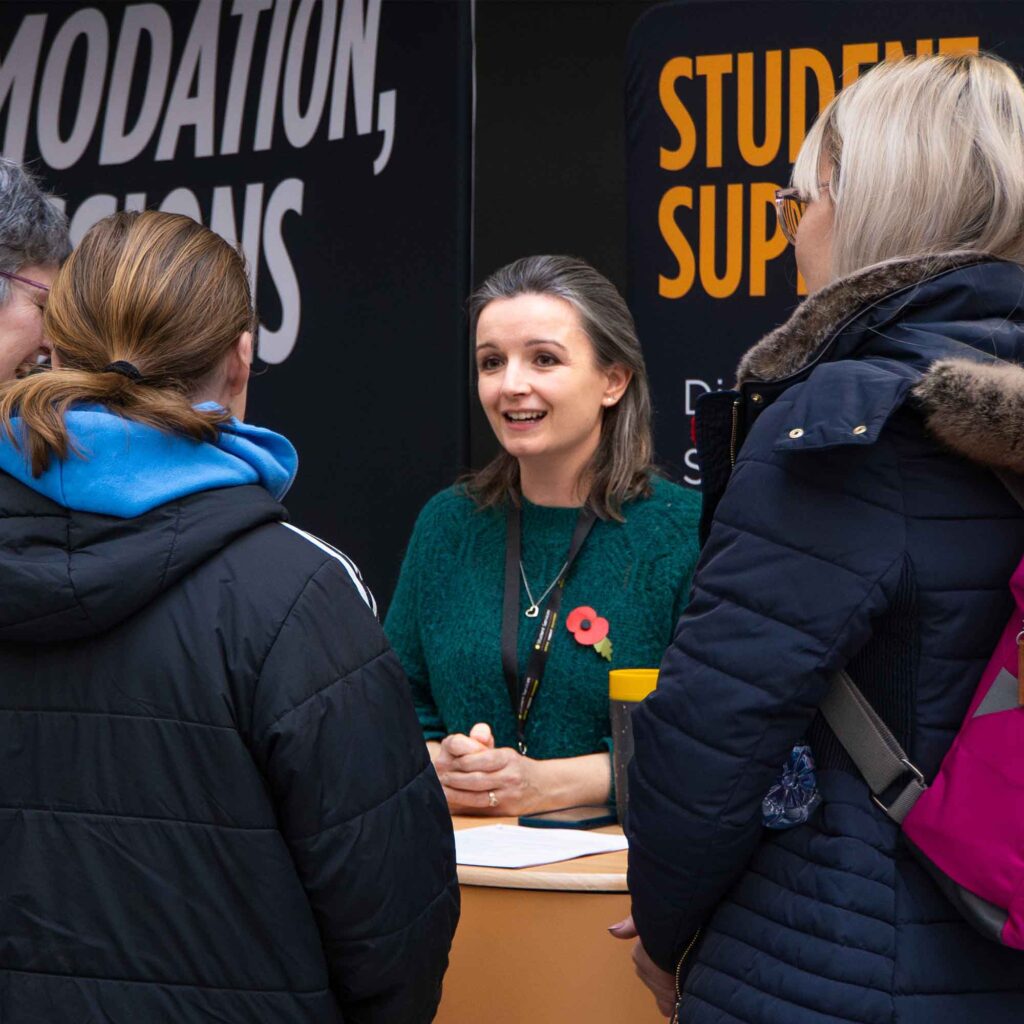 Member of student support services chatting to students at an open day.