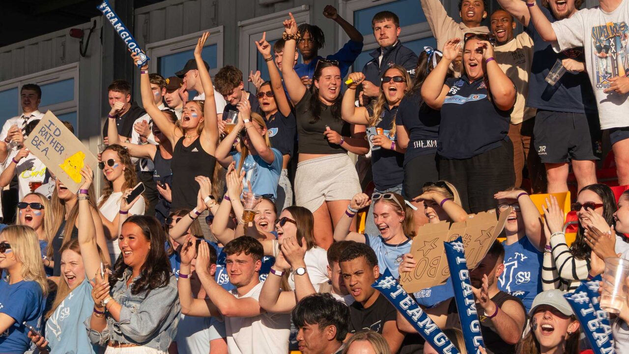 Crowds of students celebrate in the stands at a Varsity sporting event.