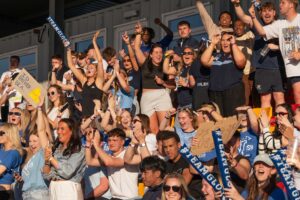 Crowds of students celebrate in the stands at a Varsity sporting event.