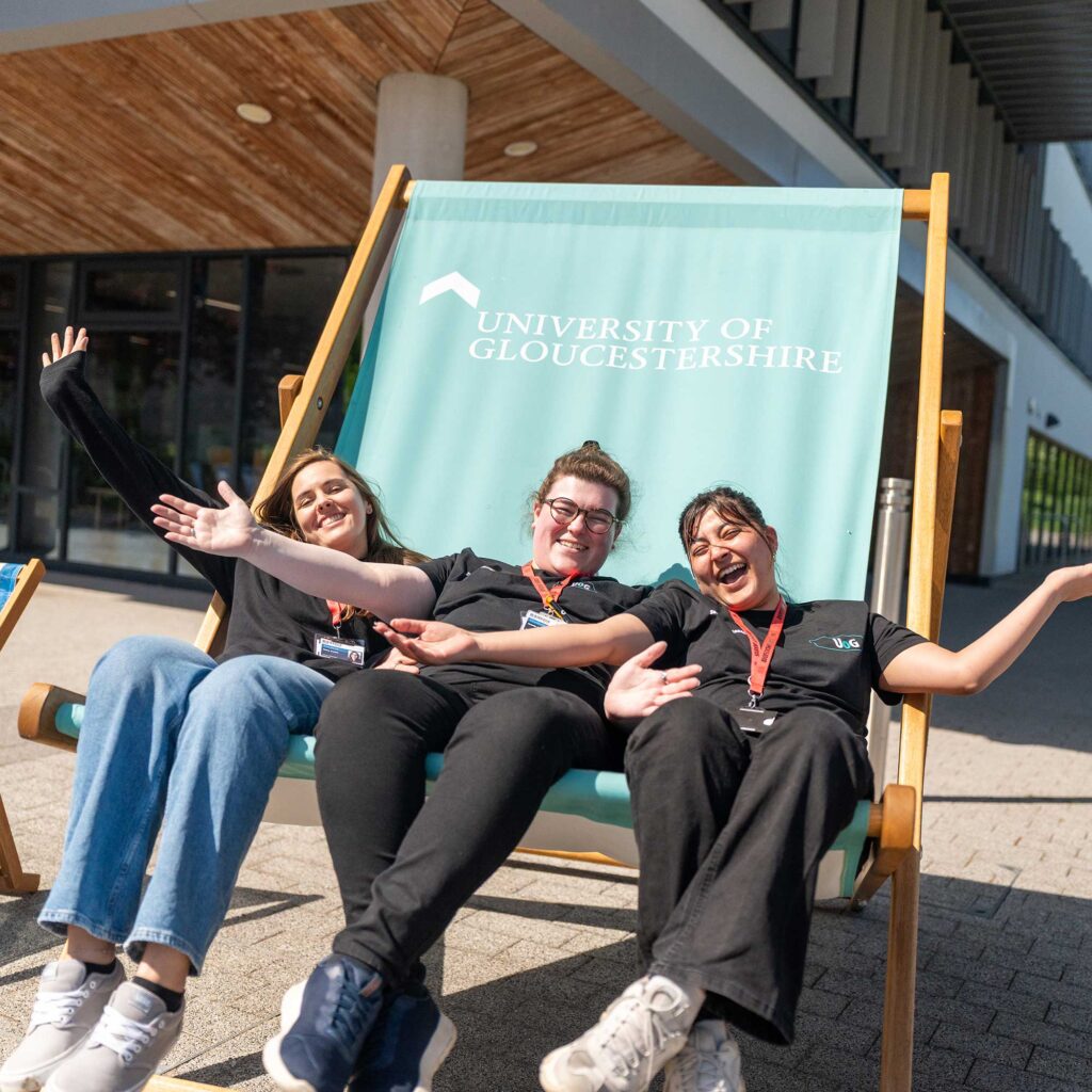 Three student ambassadors sit in a giant deckchair outside the Businses School.