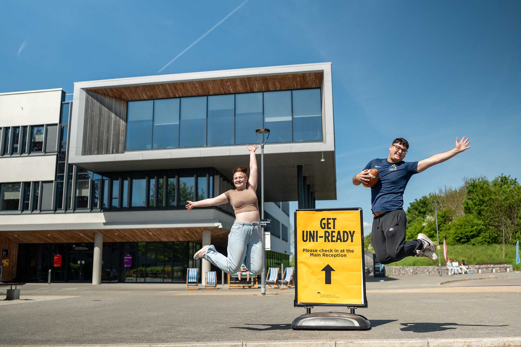 Two students jumping in celebration outside the Business School at a 'Get Uni-Ready' event.