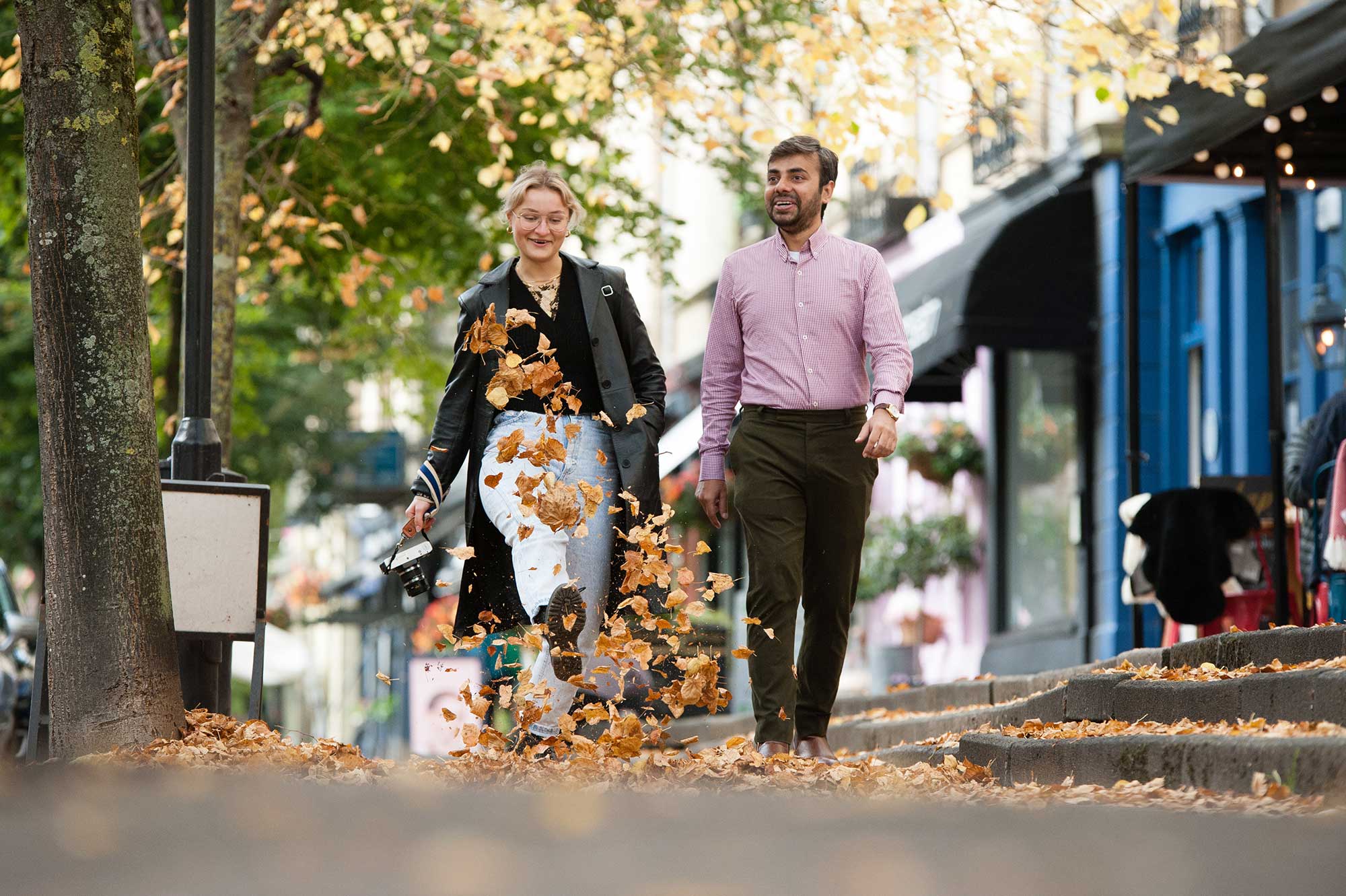 Two postgrad students walking through leaves on a tree-lined street in Cheltenham.