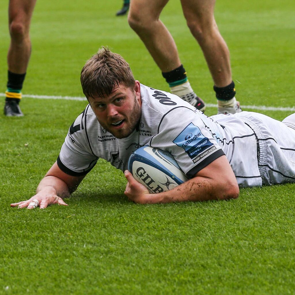 Ed Slater holding the rugby ball while lying on the pitch during a rugby game.