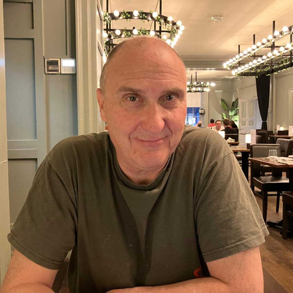 Head and shoulders photo of Sam Clark-Stone sat at a restaurant table smiling.