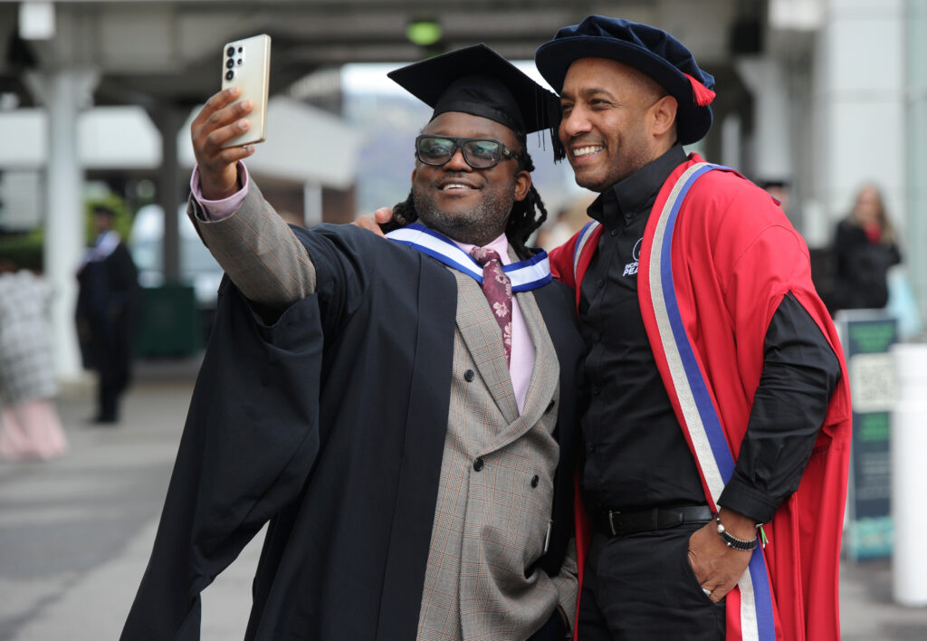 Delroy Ellis outside taking a selfie with a graduate.