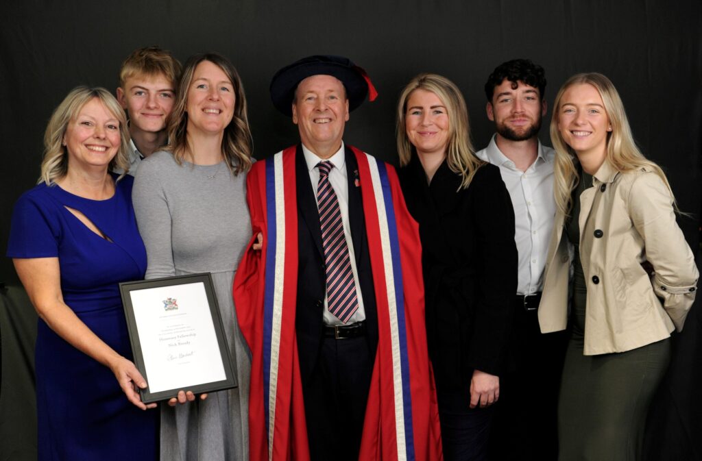 Image shows honorary fellow, Nick Broady, with his family. Nick is wearing his graduation cap and gown and his wife is holding his certificate.