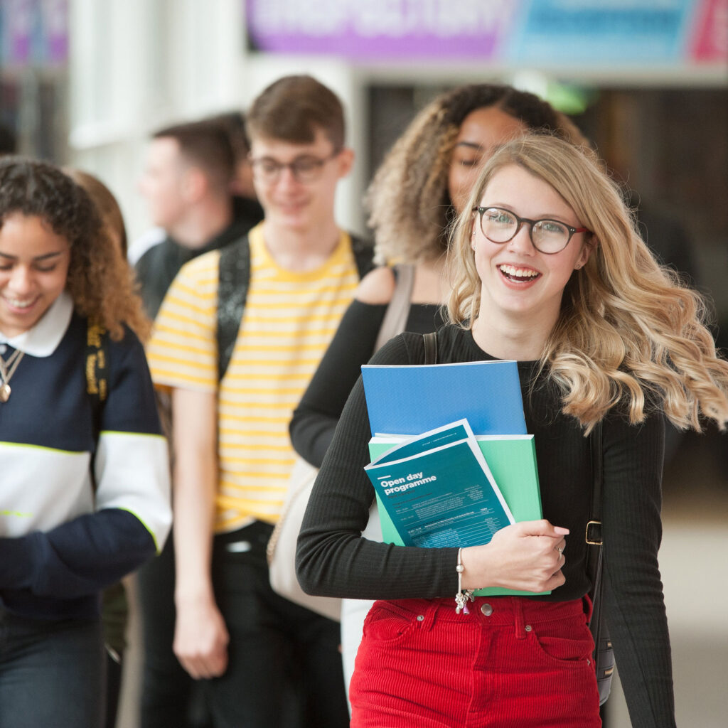 An open day attendee walks towards the camera with an open open day programme in her hand. A group of peole follow on behind her.