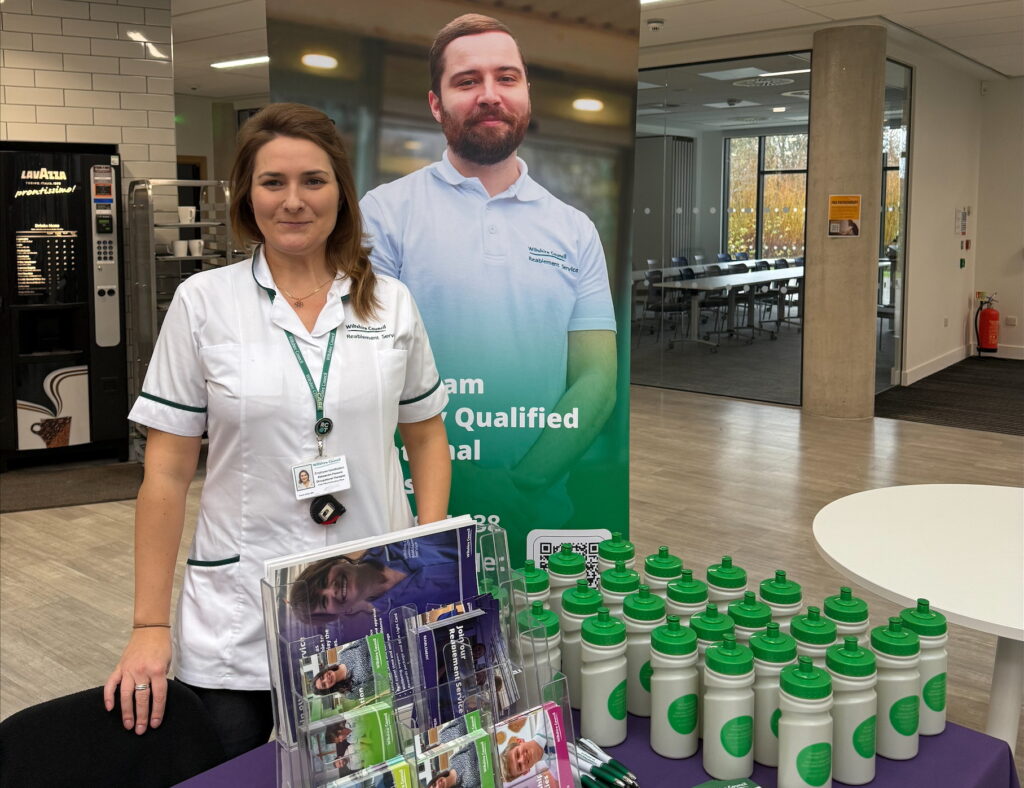 Aleksandra Parsons wearing a white top standing behind a table that has bottles on it