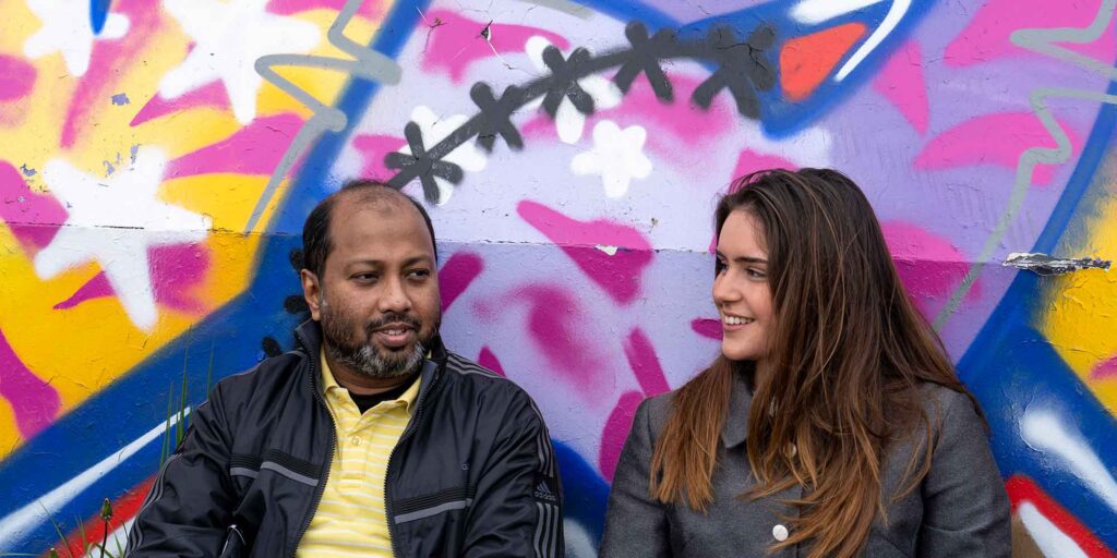 Two students leaning against a wall with grafiti on.