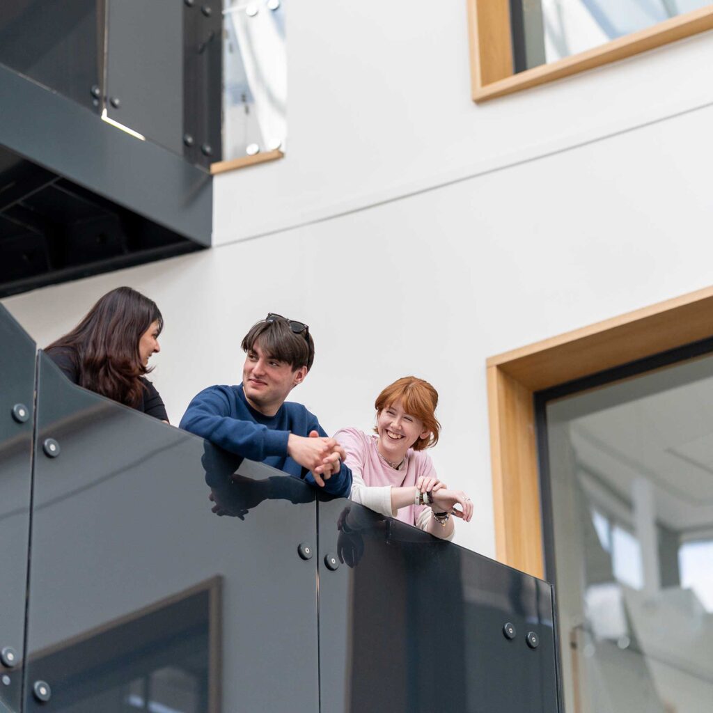 Three students overlooking an upper level in the Business School atrium.