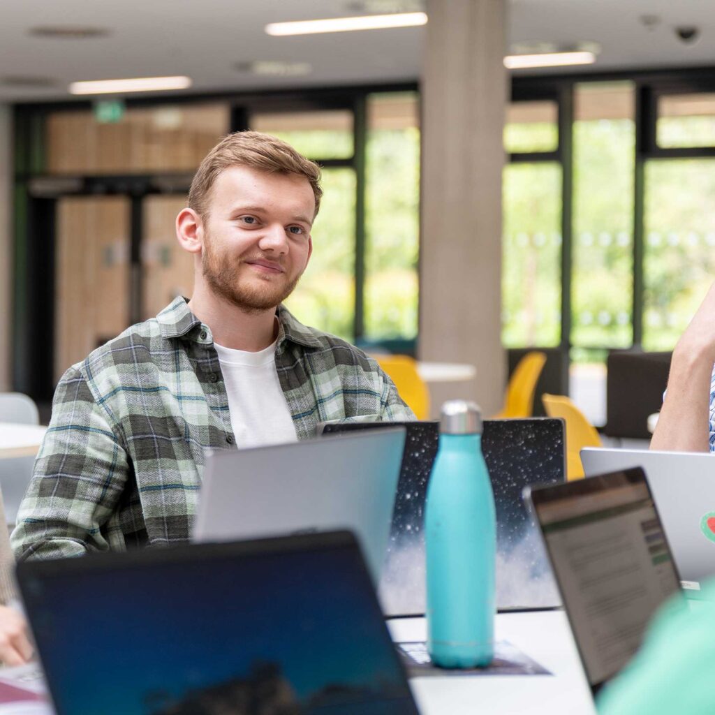 A student sitting at a table with others using laptops.