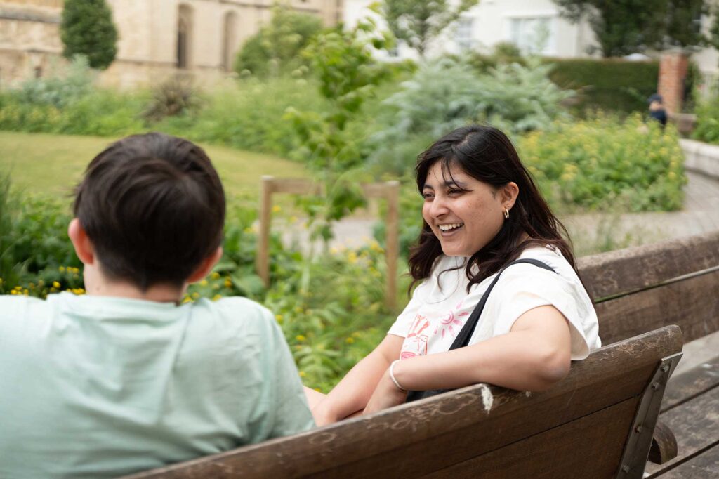 Two students sitting on a bench in the cathedral grounds talking to each other.