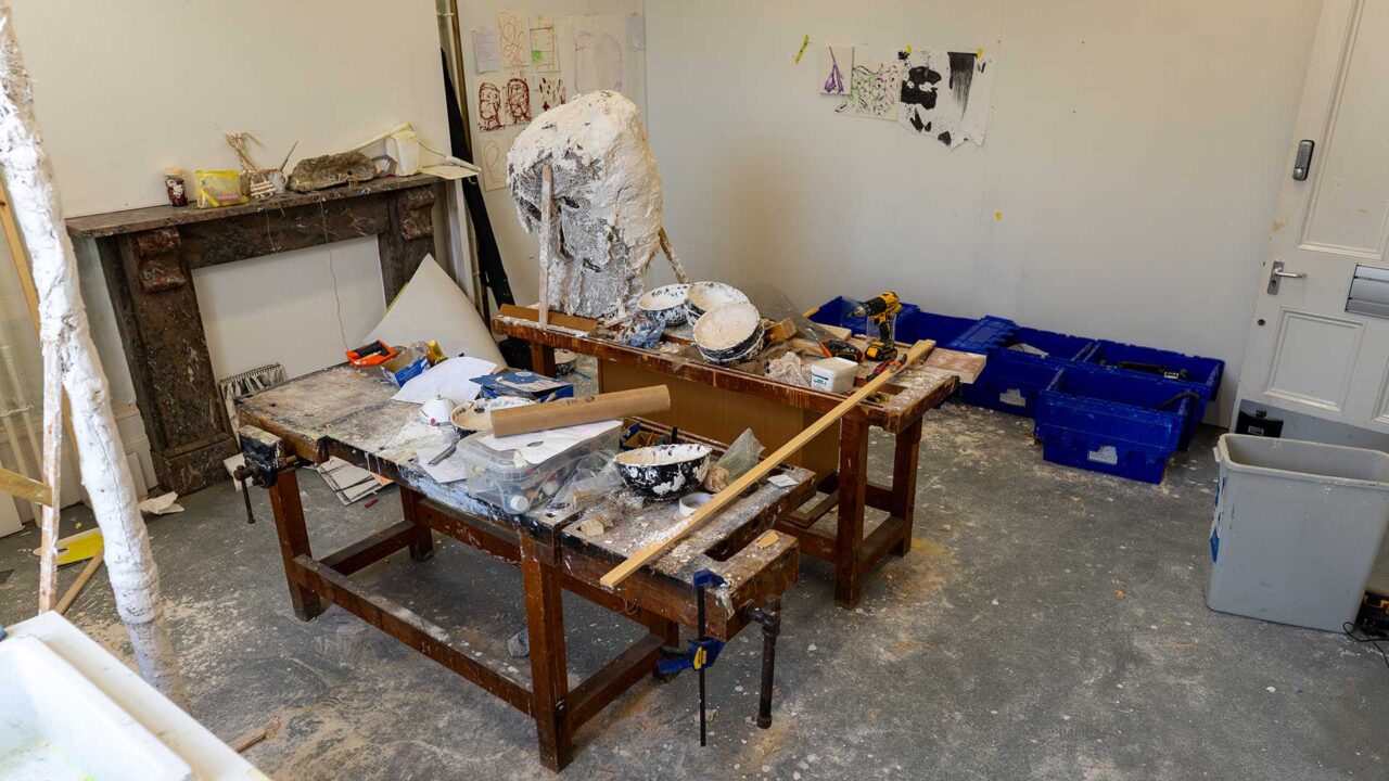 An interior of a fine art studio showing tables and pieces of artwork in progress.