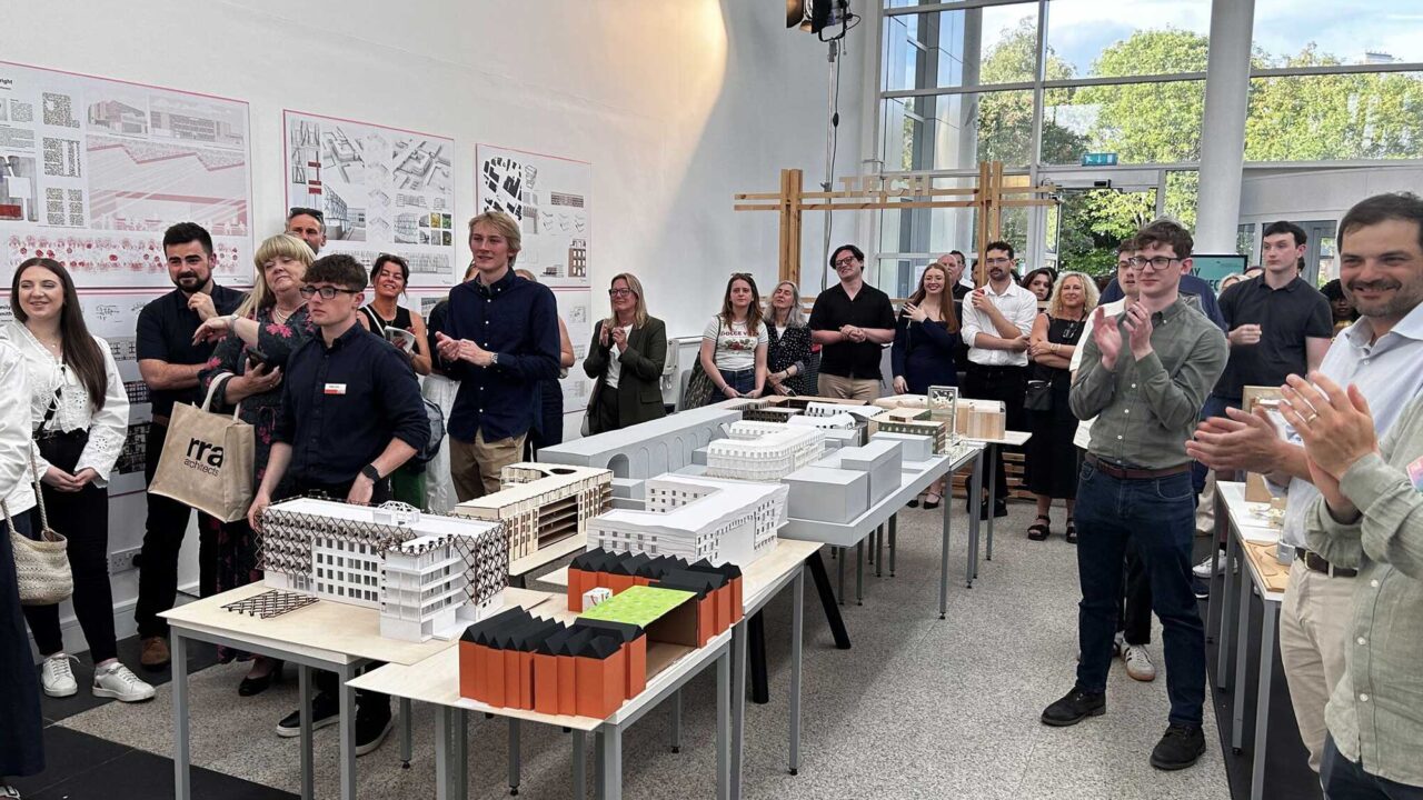 Students standing around scale models listening to a speaker.