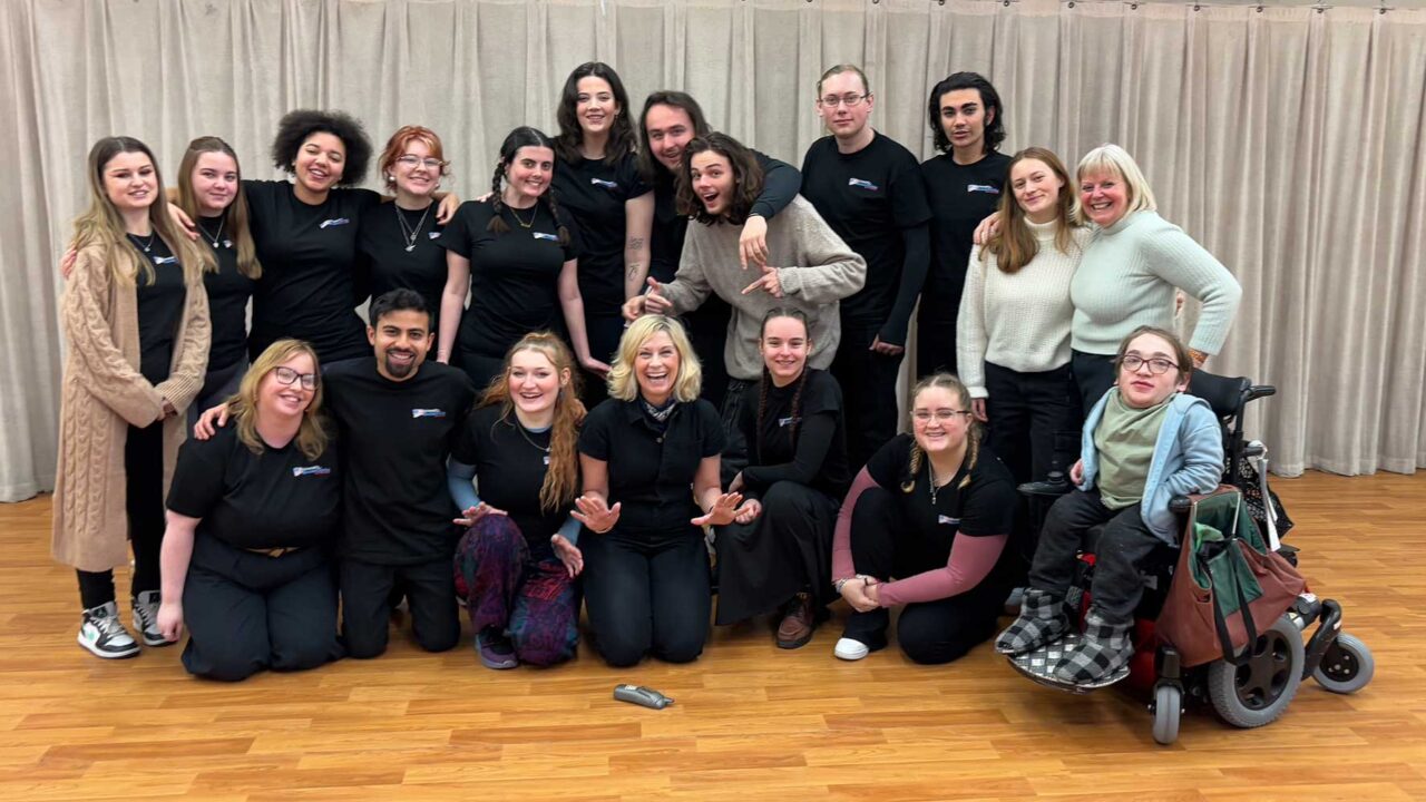 A group of musical theatre students during a rehearsal, smiling and laughing at the camera.