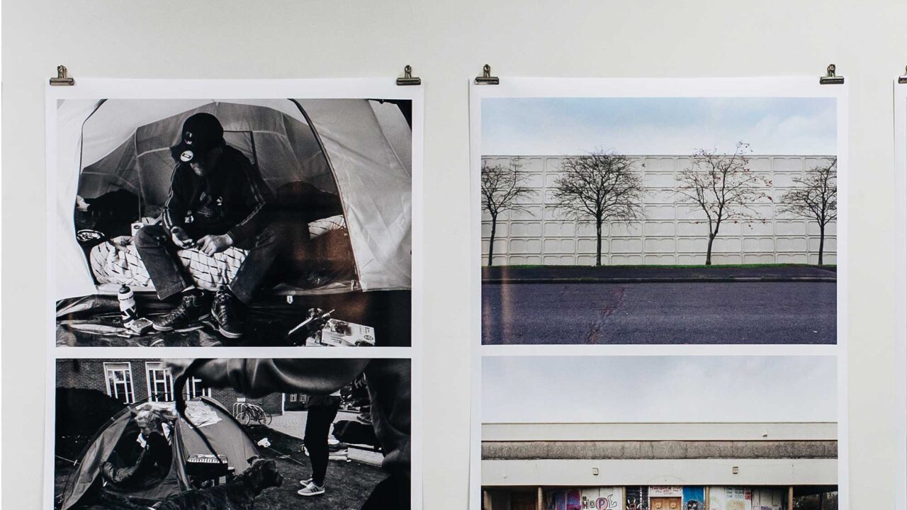 Printed photographs hanging on a wall as part of an exhibition. They're being held in place by a small bulldog clip in each corner.