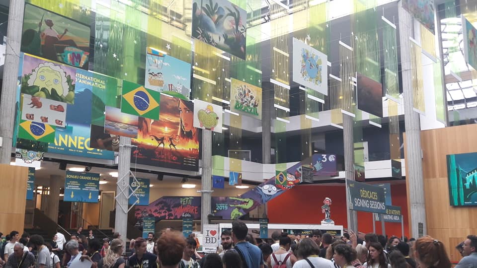 An atrium at the Annecy International Animation Film Festival showing poster banners and people talking.