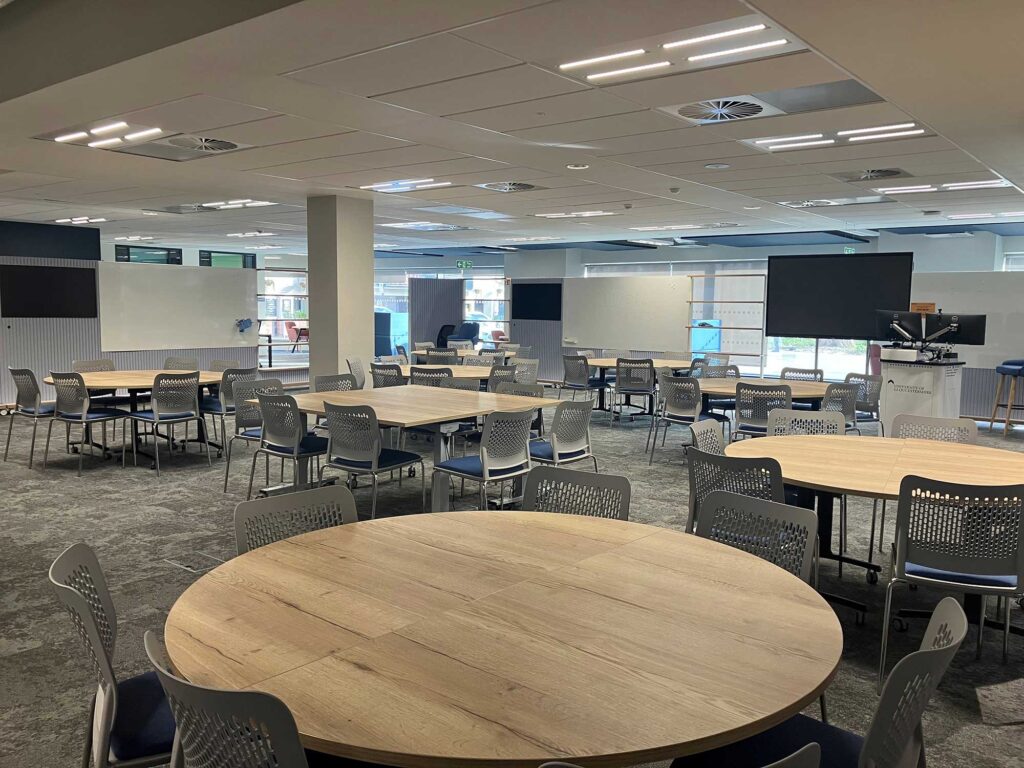 A large open-plan space showing tables, chairs and screens.
