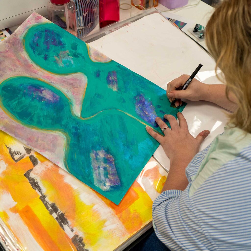 Student working on a piece of art and signing it in the bottom right hand corner.