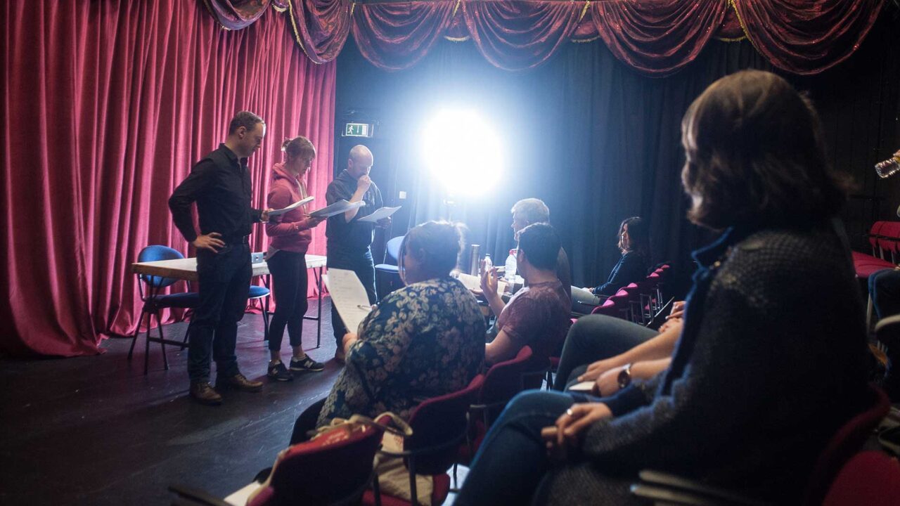 Creative writing students in the audience of the Everyman Theatre watching actors perform their scripts.