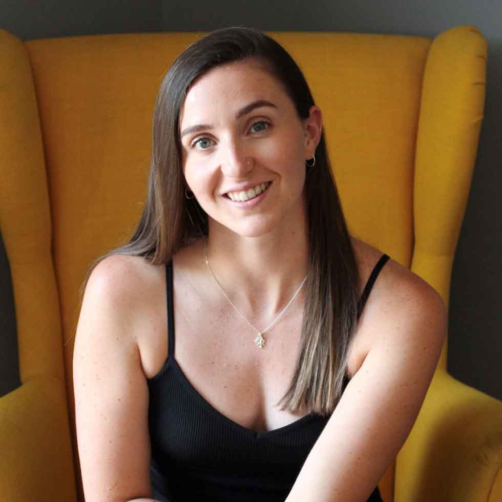 A photo of Fiona sat on a yellow chair smiling.