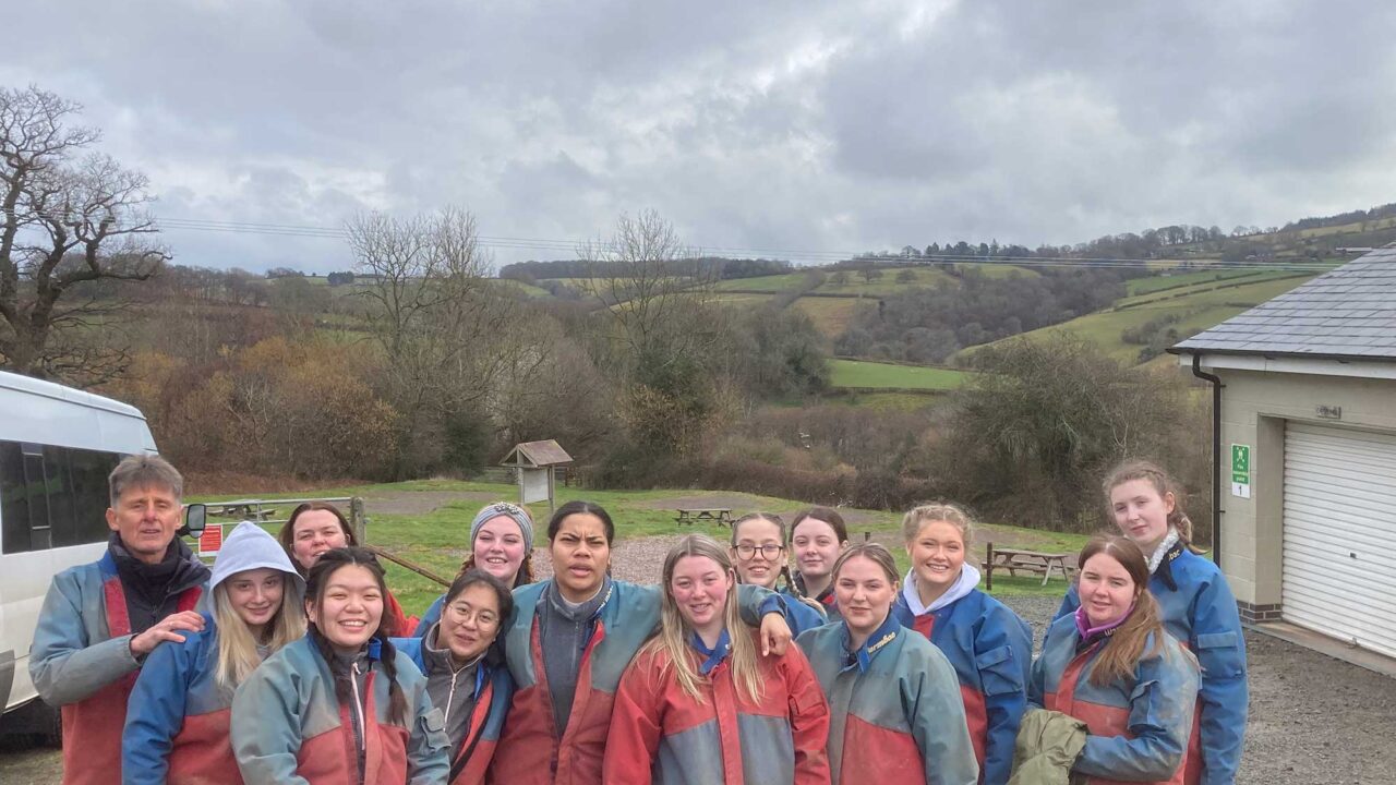 A group of Education students wear matching overalls on a trip in the countryside.