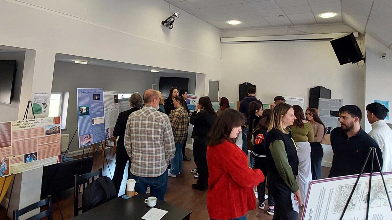 A group of students and staff looking at poster displays on student dissertation projects.