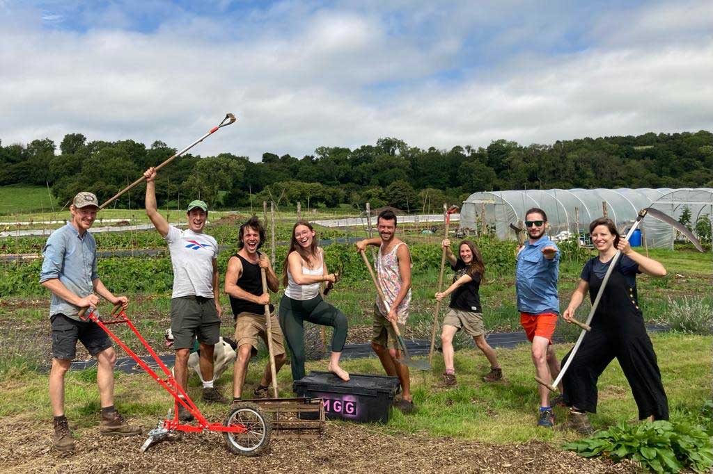 A group of students holding gardening tools posing for a photo on an allotment.