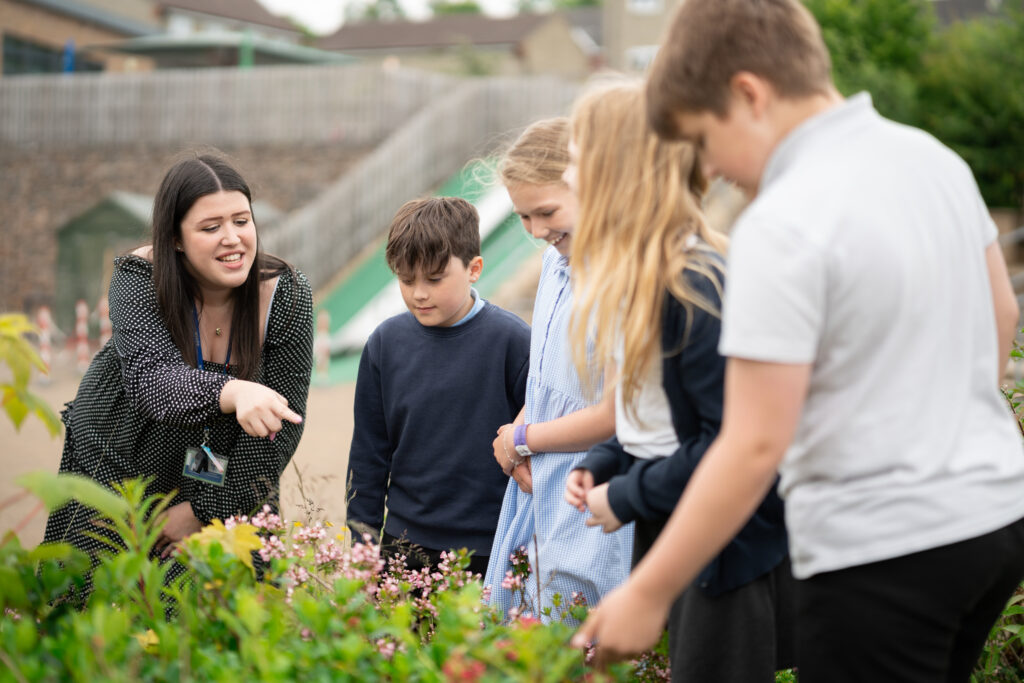 Teacher training student with four school pupils outside looking at shrubs and plants.