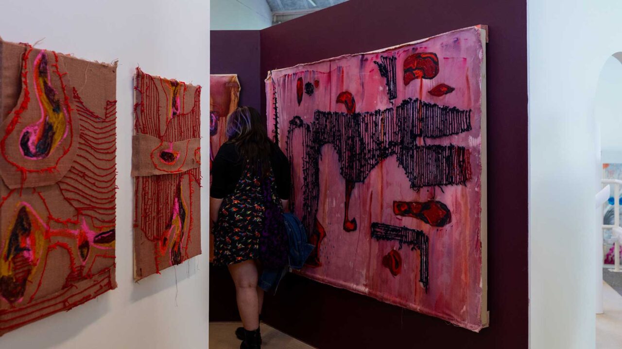 Textile blocks hanging up at the degree show with someone walking through.