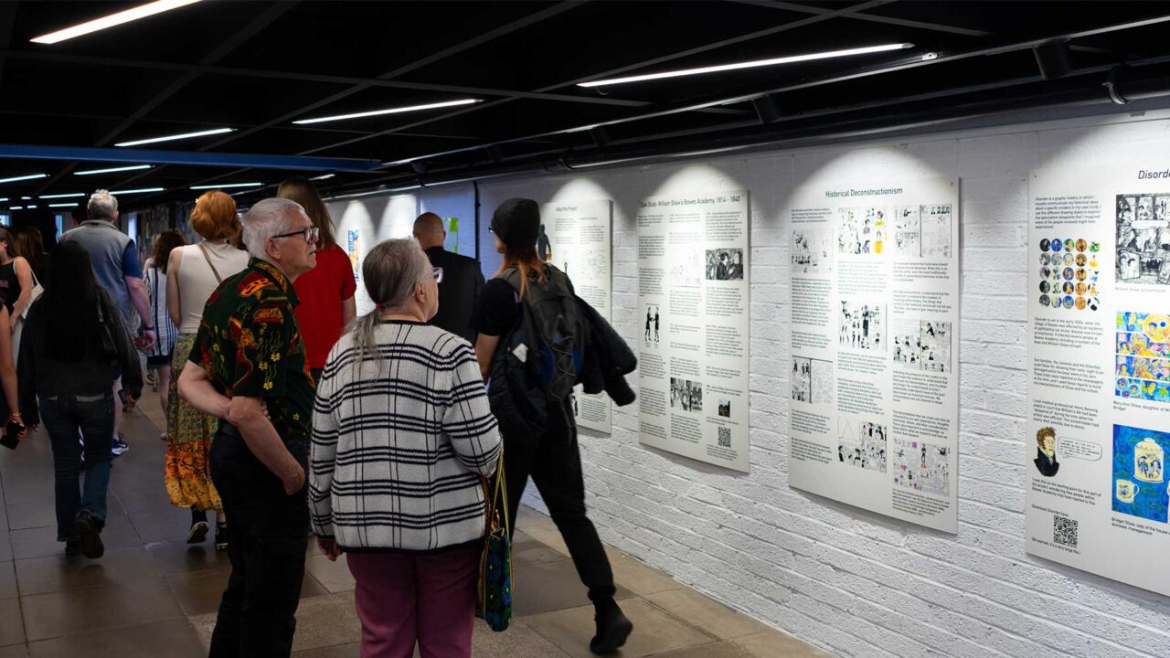 Corridor at Park Campus showing degree show work on boards and guests looking at these.