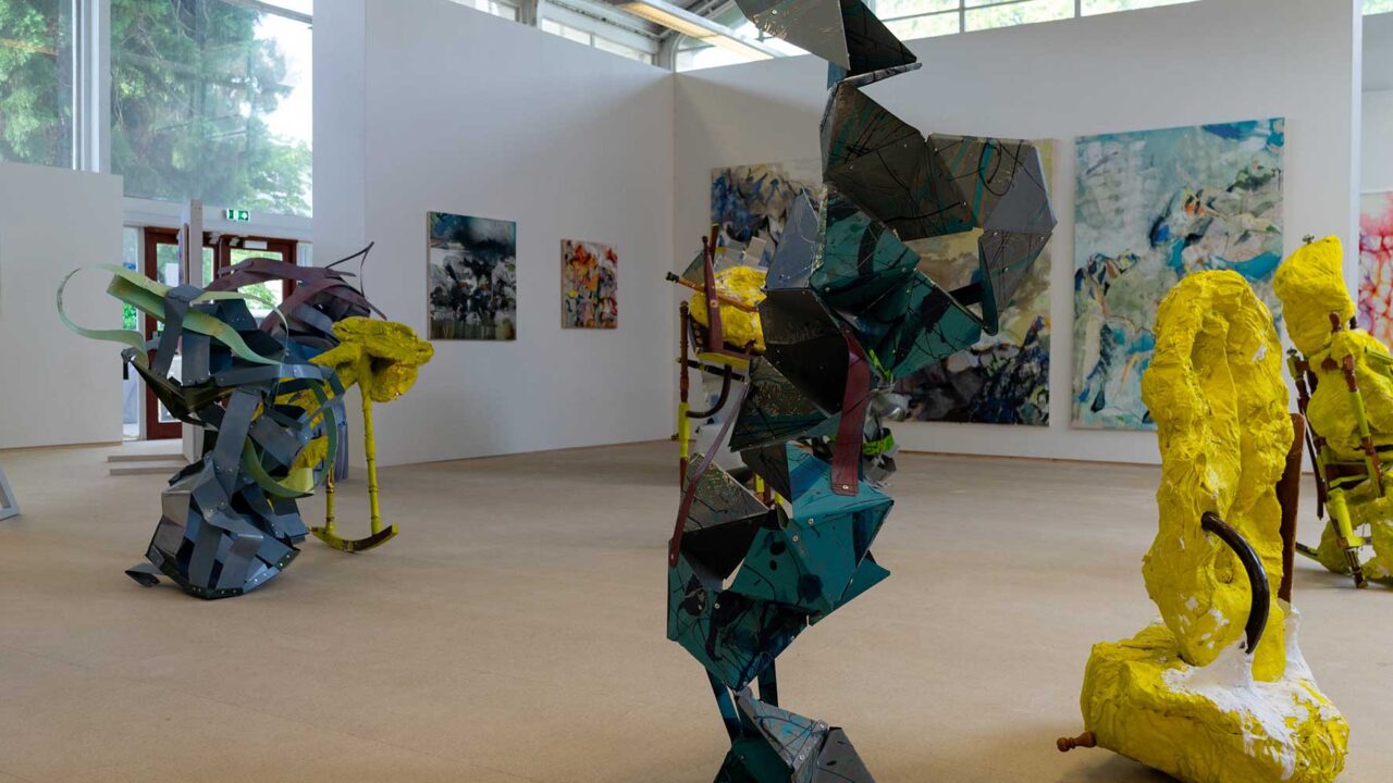 Exhibition space at Park campus with sculptures made out of different materials and large canvasses displayed in the background.