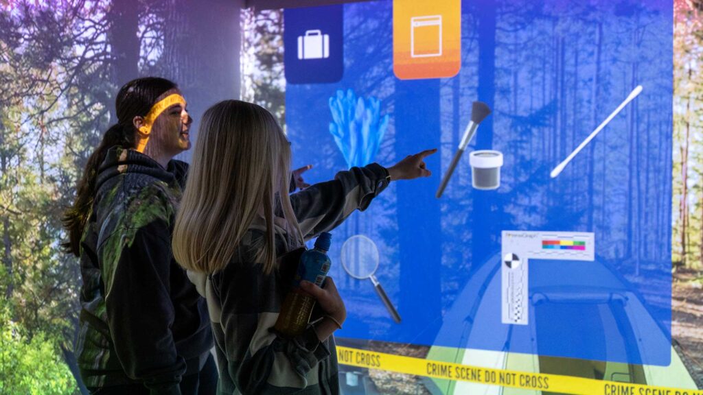 Two students pointing to the screen showing a simulated crime scene in at the FutureSim facility.