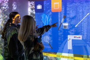 Two students pointing to the screen showing a simulated crime scene in at the FutureSim facility.
