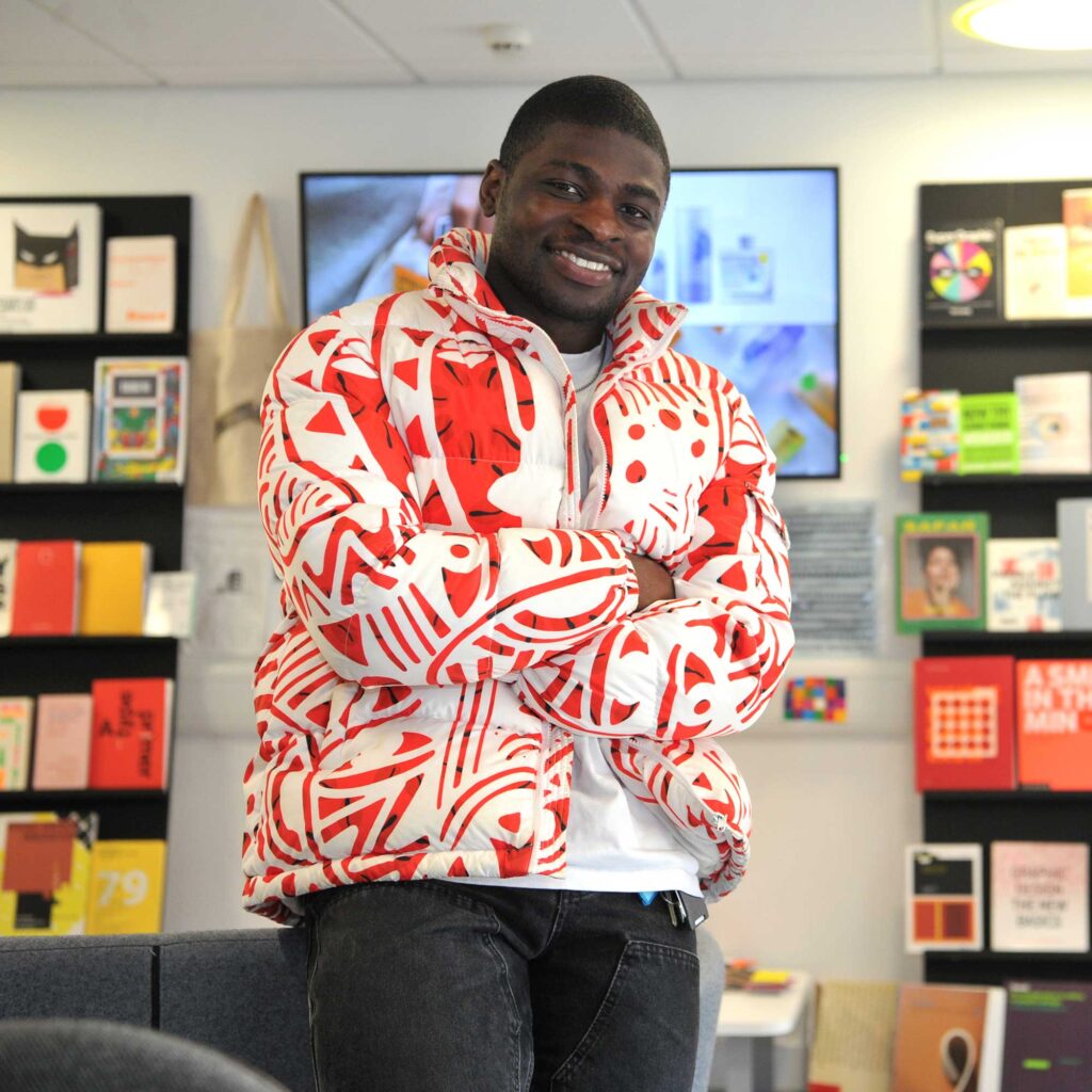 Graphic design student, Abiola, stands with his arms crossed in the studio.
