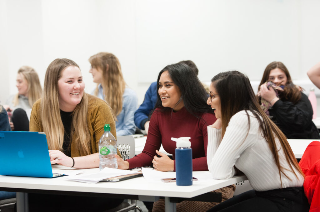 a group of smiling students sat around a table with bottles of water and a laptop