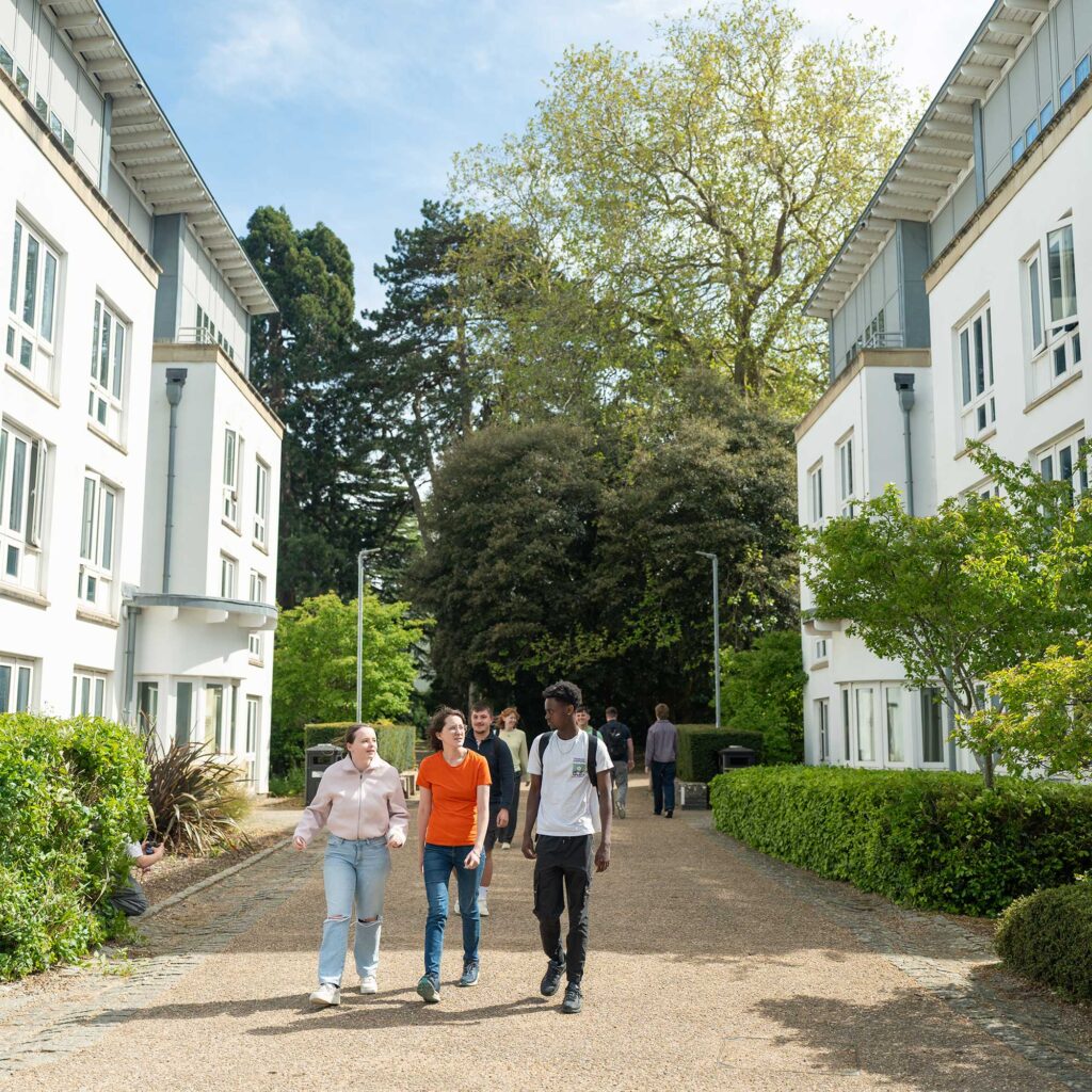 A group of students walking on a path through Park Campus in the sunshine.