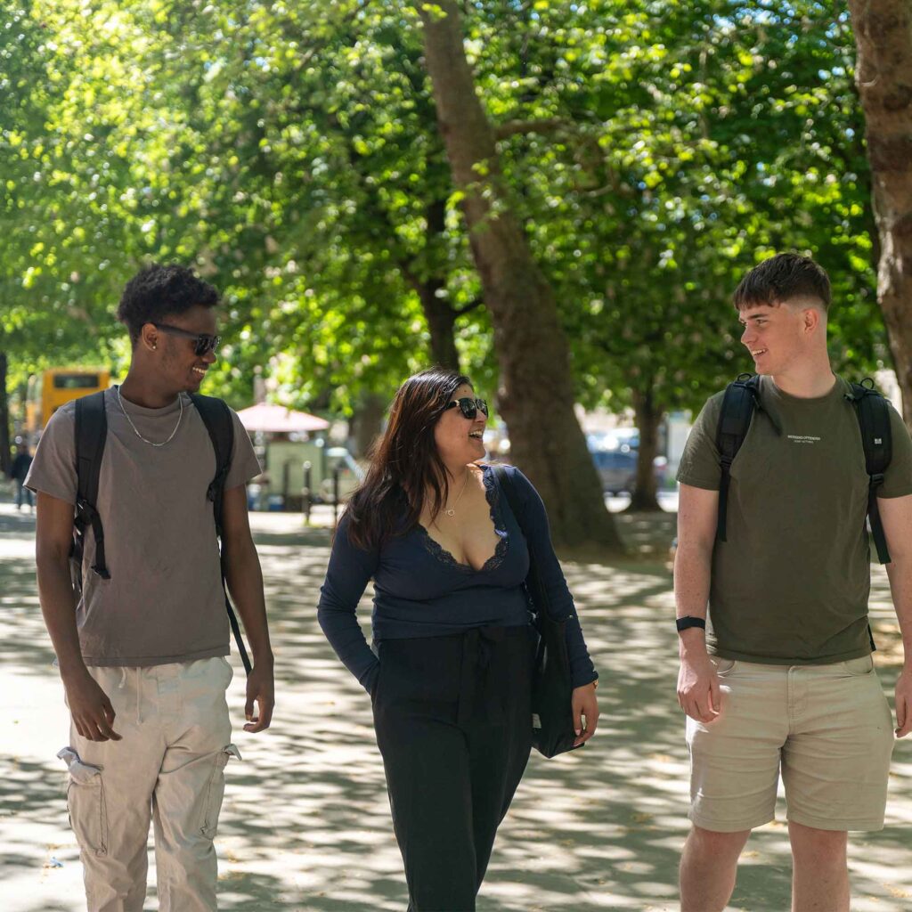 A group of three students walking through the street in Cheltenham laughing.