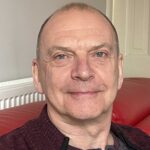 Head and shoulders shot of Geoff Layer sitting on a red chair.