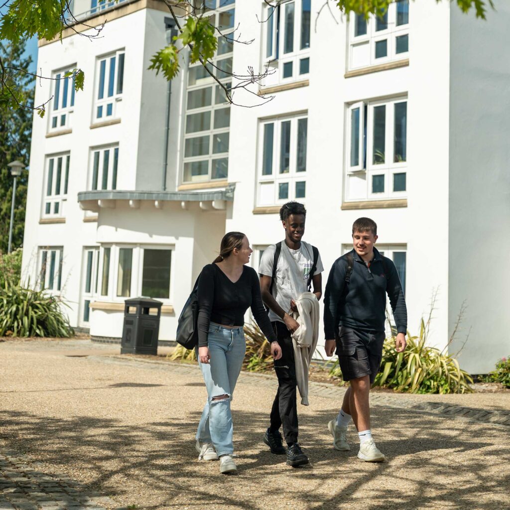 Three students walking on a path through Park Campus in the sunshine.