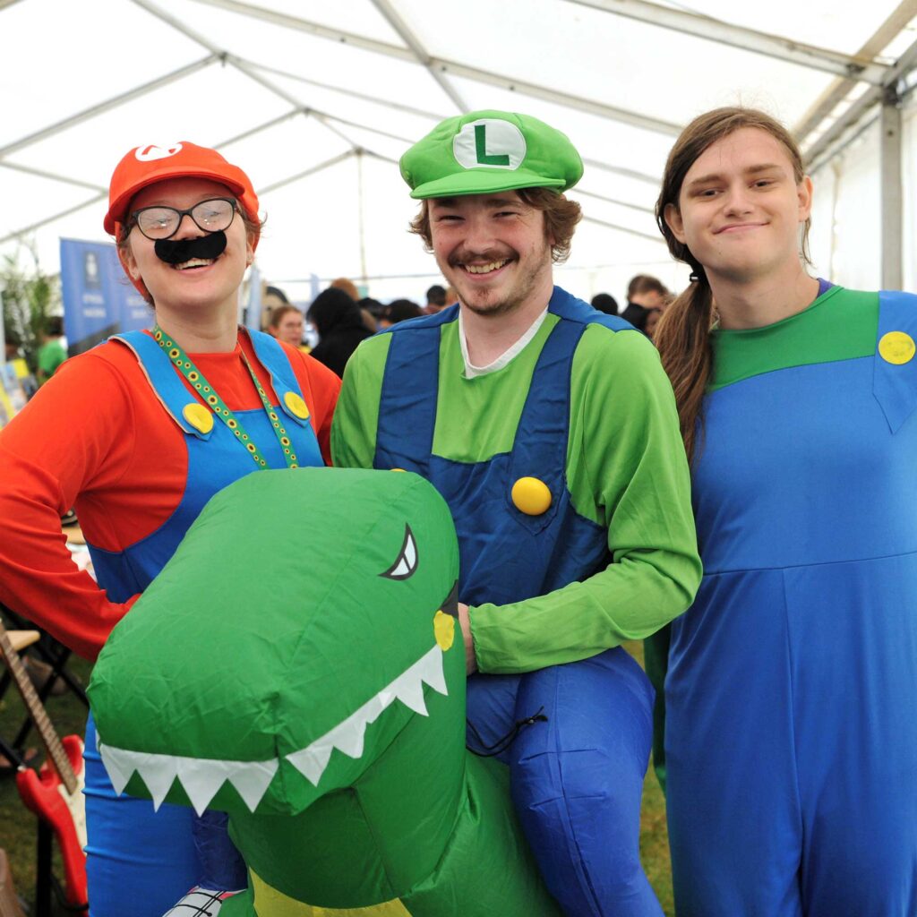 Three students dressed up as Nintendo characters, one is holding an inflatable dinosaur.