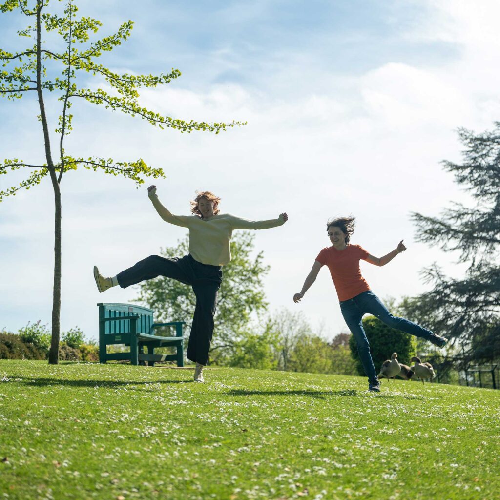 Two students jumping in the air in a celebratory way on the grass in a park.