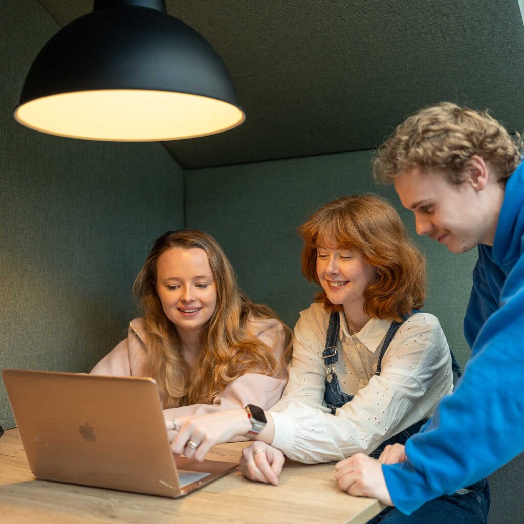 Three students look at a laptop together.