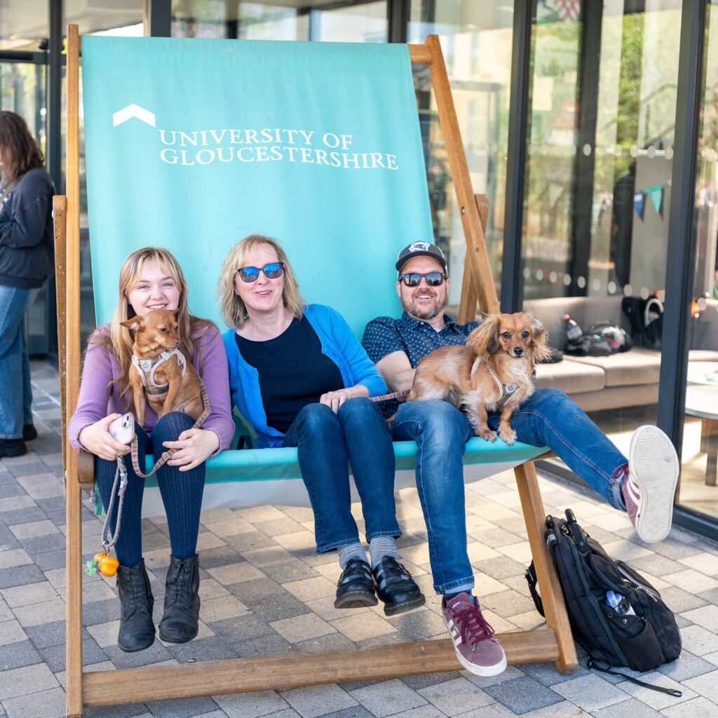A prospective student sits on the giant deck chair with her parents and two dogs.