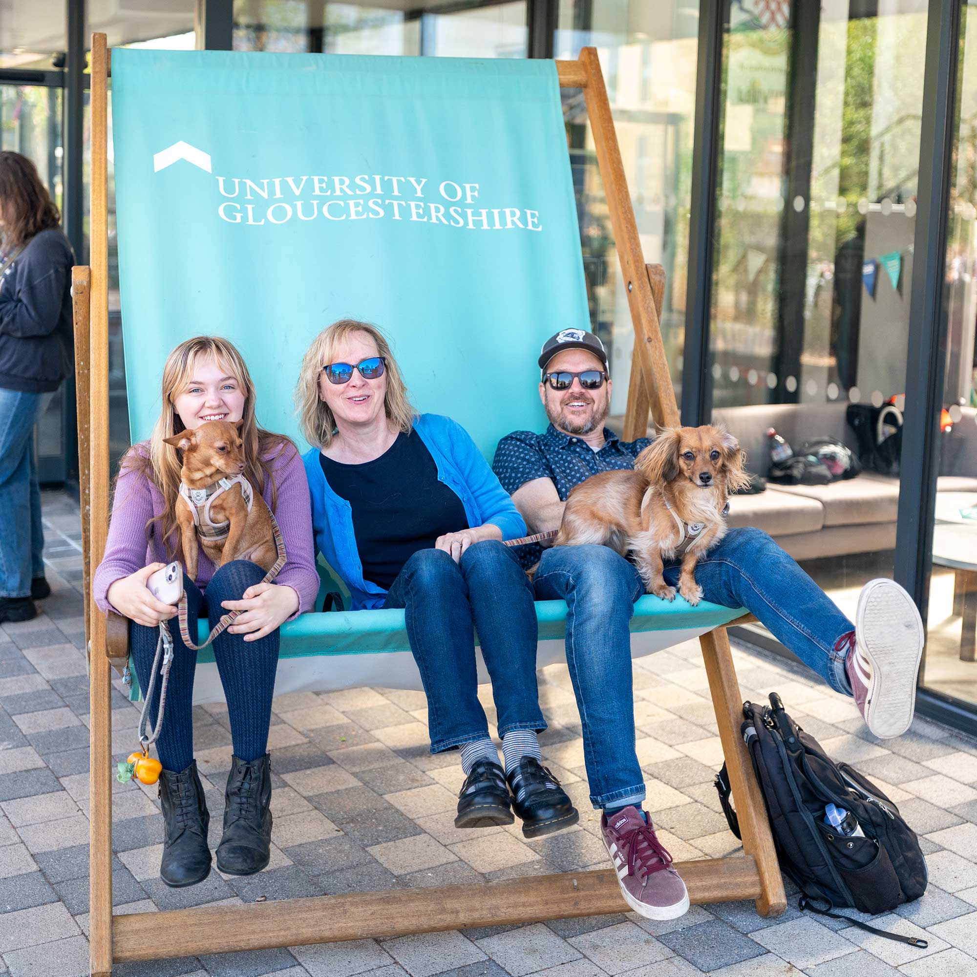 A prospective student sits on the giant deck chair with her parents and two dogs.