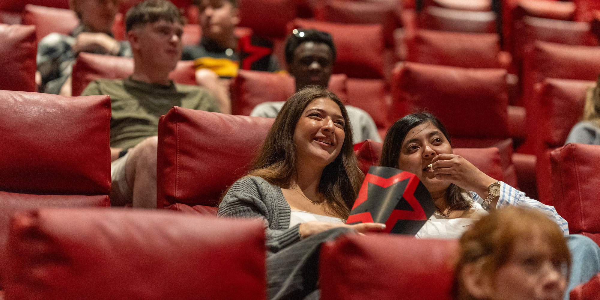 Students sitting at the cinema eating popcorn.