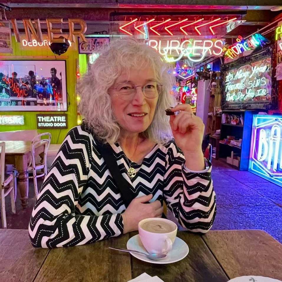 Dr Alison Harmer sitting at a table in a cafe-bar-diner with a cup of coffee.