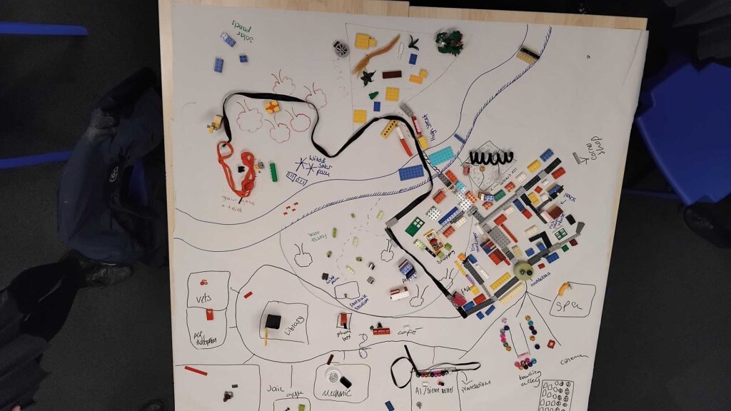 A large piece of paper showing the layout of a town with a number of items such as Lego bricks laid on it.