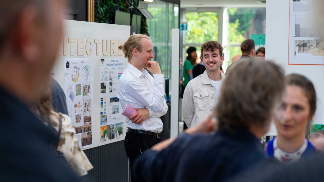 Students and guests gather to look at display boarding showing architecture displays at the Degree Show.
